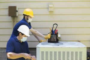 two-techs-wearing-face-masks-working-on-air-conditioner-outside-unit