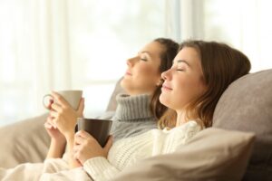 two-women-leaning-back-on-couch-with-mugs-looking-comfortable